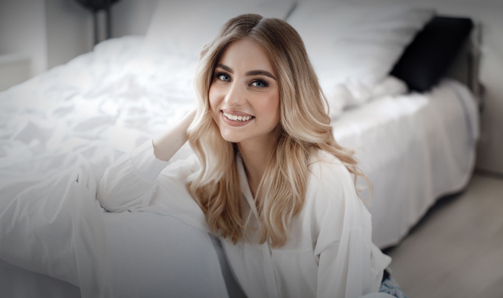 Smiling woman sitting on bed, bright atmosphere.